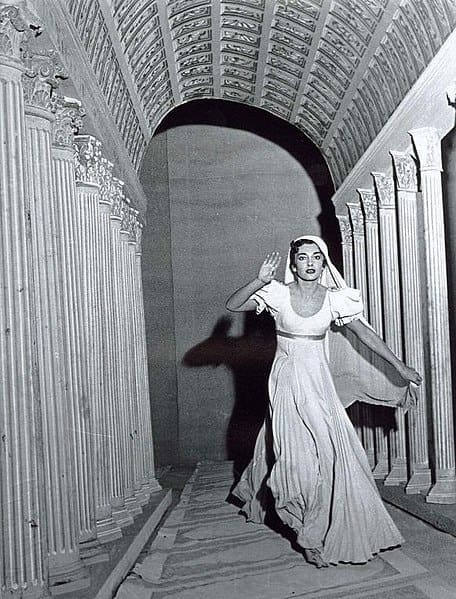 A woman in white dress walking through an archway.